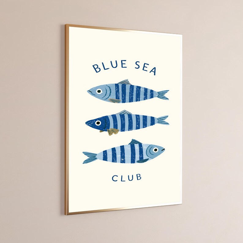 Pode incluir: Uma impress&atilde;o de arte de parede retangular num fundo creme com tr&ecirc;s peixes listrados azuis alinhados horizontalmente. O texto "BLUE SEA" est&aacute; impresso a azul acima dos peixes e a palavra "CLUB" est&aacute; impressa a azul abaixo.