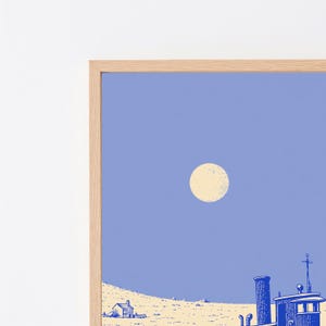 May include: A framed art print featuring a light blue sky with a pale yellow circular moon above a landscape. The scene includes a small house and a blue industrial structure with a chimney and a mast, rendered in a stylized, graphic illustration.