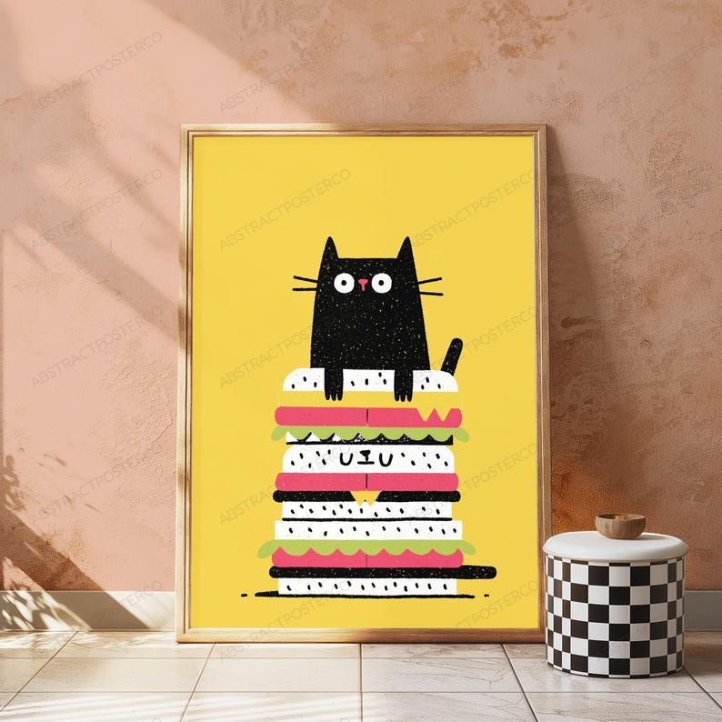 May include: A framed wall art print featuring a black cat with wide eyes sitting atop a tall, multi-layered sandwich illustration against a solid yellow background. The sandwich includes layers of white bread, pink meat, and green lettuce.