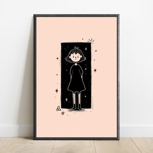 May include: A framed wall art print featuring a black and white line drawing of a person with short hair wearing a dress, centred within a black rectangular border on a pale peach background, surrounded by small star and circular graphic accents.