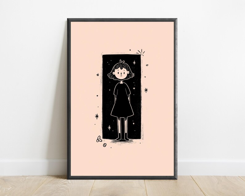 May include: A framed wall art print featuring a black and white line drawing of a person with short hair wearing a dress, centred within a black rectangular border on a pale peach background, surrounded by small star and circular graphic accents.