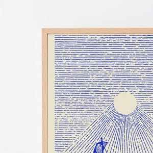 May include: A framed wall art print featuring a blue line-art illustration of a sailboat on water beneath a large, solid cream-coloured sun. The design uses horizontal blue lines for the sky and radiating diagonal lines for the water, all set in a light wood frame.