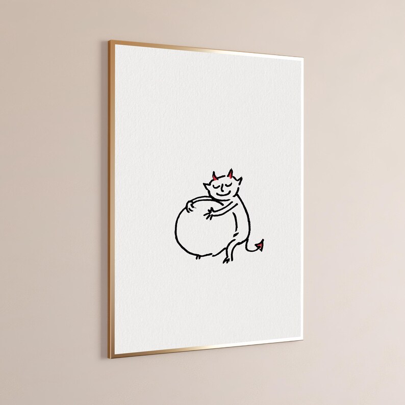 May include: A framed wall art print featuring a simple black line drawing of a small creature with red horns and a red-tipped tail, smiling while hugging a large round shape, set against a plain white background within a thin gold frame.