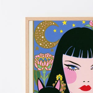 May include: A framed art print featuring a stylized illustration of a person with black hair, blue eyes, and red lips. The background is a vibrant blue sky with a gold crescent moon, yellow stars, and a pink flower. The frame is light wood.