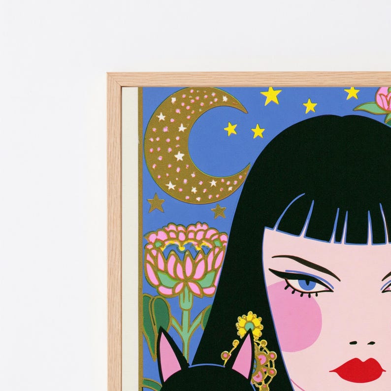 May include: A framed art print featuring a stylized illustration of a person with black hair, blue eyes, and red lips. The background is a vibrant blue sky with a gold crescent moon, yellow stars, and a pink flower. The frame is light wood.