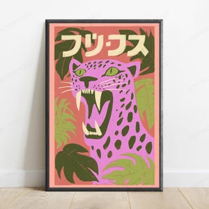 May include: A framed wall art print featuring a pink leopard with dark spots and green eyes, roaring with visible fangs. The background is a salmon-colored field with dark green tropical leaves and Japanese text at the top in a cream color.