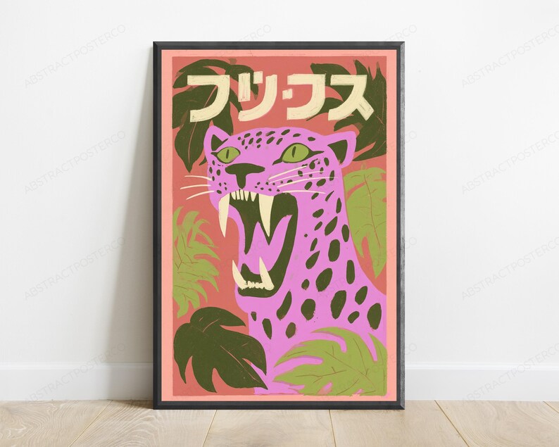 May include: A framed wall art print featuring a pink leopard with dark spots and green eyes, roaring with visible fangs. The background is a salmon-colored field with dark green tropical leaves and Japanese text at the top in a cream color.