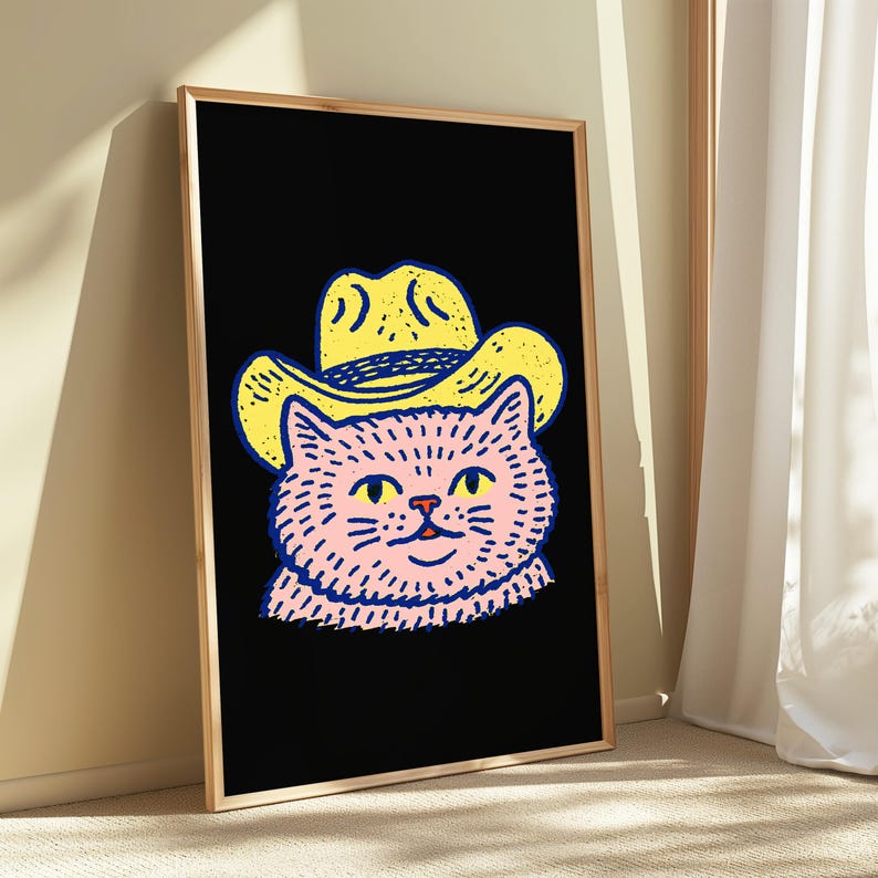 Puede incluir: Una impresi&oacute;n de arte mural rectangular enmarcada que presenta una ilustraci&oacute;n gr&aacute;fica de un gato rosa con un sombrero de vaquero amarillo. El gato tiene ojos amarillos y contornos azul oscuro sobre un fondo negro s&oacute;lido en un marco de madera clara.