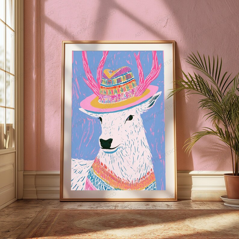K&ouml;nnte beinhalten: Ein gerahmter Kunstdruck, der einen stilisierten wei&szlig;en Hirsch mit rosa Geweih zeigt, der einen farbenfroh gemusterten Hut mit breiter rosa Krempe und ein passendes gestreiftes Halstuch tr&auml;gt, vor einem leuchtend blauen Hintergrund.