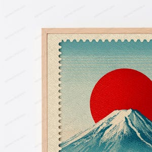 K&ouml;nnte beinhalten: Ein gerahmter Wandkunstdruck mit einem Briefmarkendesign und einem strukturierten cremefarbenen Rand. Die zentrale Grafik zeigt einen gro&szlig;en, soliden roten Kreis, der die Sonne &uuml;ber einem blauen Berggipfel mit wei&szlig;en Schneekappen darstellt.