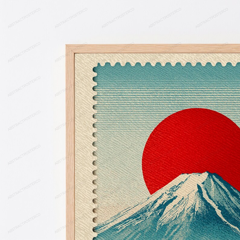 K&ouml;nnte beinhalten: Ein gerahmter Wandkunstdruck mit einem Briefmarkendesign und einem strukturierten cremefarbenen Rand. Die zentrale Grafik zeigt einen gro&szlig;en, soliden roten Kreis, der die Sonne &uuml;ber einem blauen Berggipfel mit wei&szlig;en Schneekappen darstellt.