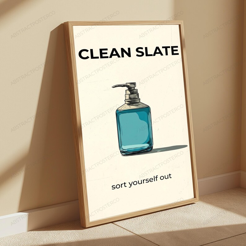 May include: A framed wall art print featuring a light cream background with the text CLEAN SLATE at the top and sort yourself out at the bottom. In the center is a hand-drawn illustration of a square soap dispenser filled with blue liquid.