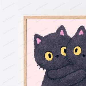 Pode incluir: Uma impress&atilde;o de arte emoldurada apresentando dois gatos felpudos cinza-escuros com grandes olhos amarelos e orelhas internas cor-de-rosa, abra&ccedil;ando-se contra um fundo rosa claro. A obra est&aacute; em uma moldura de madeira de tom claro.