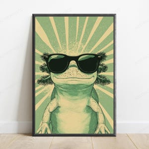 May include: A framed wall art print featuring a green axolotl wearing black sunglasses. The axolotl is centered against a background of radiating light green and cream-colored sunburst lines, creating a graphic illustration with a distinct color palette.