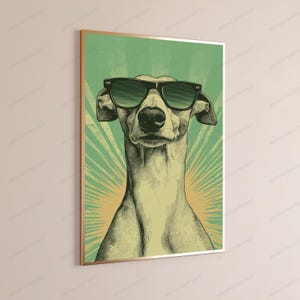 May include: A framed wall art print featuring a stylized illustration of a greyhound dog wearing black sunglasses. The dog is centered against a green and yellow sunburst background with a vintage-inspired texture and a thin metallic frame.