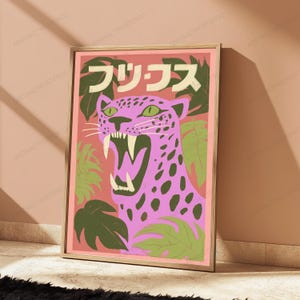 May include: A framed wall art print featuring a pink leopard with dark spots and an open mouth showing sharp teeth. The background is a salmon color with green tropical leaves. At the top, there is Japanese text in white characters.