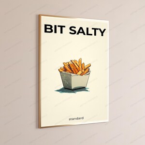 May include: A rectangular wall art print featuring a cream background with the black text BIT SALTY at the top and standard at the bottom. In the center, a hand-drawn illustration depicts a portion of golden-brown french fries in a white container.