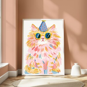 K&ouml;nnte beinhalten: Ein gerahmter Kunstdruck, der eine flauschige Katze mit langem rosa und gelbem Fell zeigt. Die Katze tr&auml;gt einen blauen Partyhut mit roten Punkten und eine gelb umrandete Sonnenbrille mit dunklen Gl&auml;sern. Die Illustration zeigt sichtbare Pinselstriche.