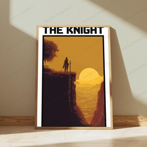 May include: A rectangular wall art print in a light wood frame featuring the text THE KNIGHT in black pixelated font. The illustration depicts a silhouette of a knight holding a sword on a cliff edge overlooking a golden sunset landscape.