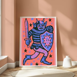 May include: A framed art print featuring a stylized illustration of a horned creature in dark blue, holding a sword and a shield with a skull emblem. The background is a vibrant coral pink color decorated with scattered blue and black stars and circles.