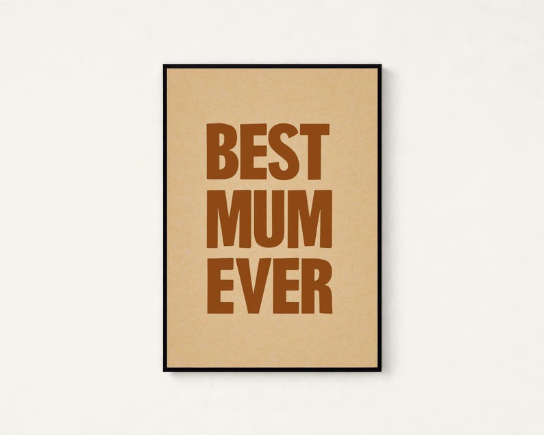 May include: A framed print with the words "BEST MUM EVER" in brown block letters on a tan background. The print is in a black frame and is centered on a white wall.