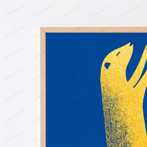K&ouml;nnte beinhalten: Ein gerahmter Wandkunstdruck mit einem tiefblauen Hintergrund und einer stilisierten, texturierten goldgelben abstrakten Form, die einer Tiersilhouette &auml;hnelt. Das Kunstwerk ist in einem hellen Holzrahmen mit schlichtem Randdesign gefasst.