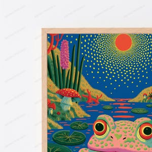 May include: A framed art print featuring a pink frog with large eyes in the foreground, overlooking a blue pond with lily pads. The landscape includes a red sun, a red-capped mushroom, and a tall pink flower against a dark blue sky.