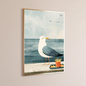 May include: A framed wall art print featuring a white and gray seagull standing on a wooden pier next to a small orange container filled with yellow french fries. The background shows a blue ocean and a pale sky with three small black birds.
