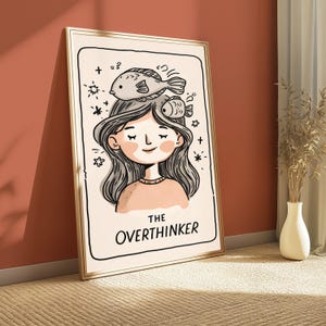 K&ouml;nnte beinhalten: Ein gerahmter Kunstdruck mit einer Cartoon-Illustration einer Person mit langem Haar und zwei Fischen auf dem Kopf. Das Kunstwerk enth&auml;lt den Text THE OVERTHINKER in schwarzen Gro&szlig;buchstaben am unteren Rand, umgeben von kleinen Sternsymbolen.