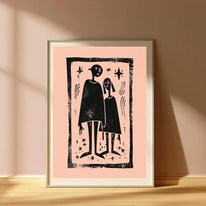 May include: A framed wall art print featuring a black ink block-print style illustration of two stylized figures standing side-by-side. The figures are surrounded by small star shapes and curved lines, all set against a solid light peach background.