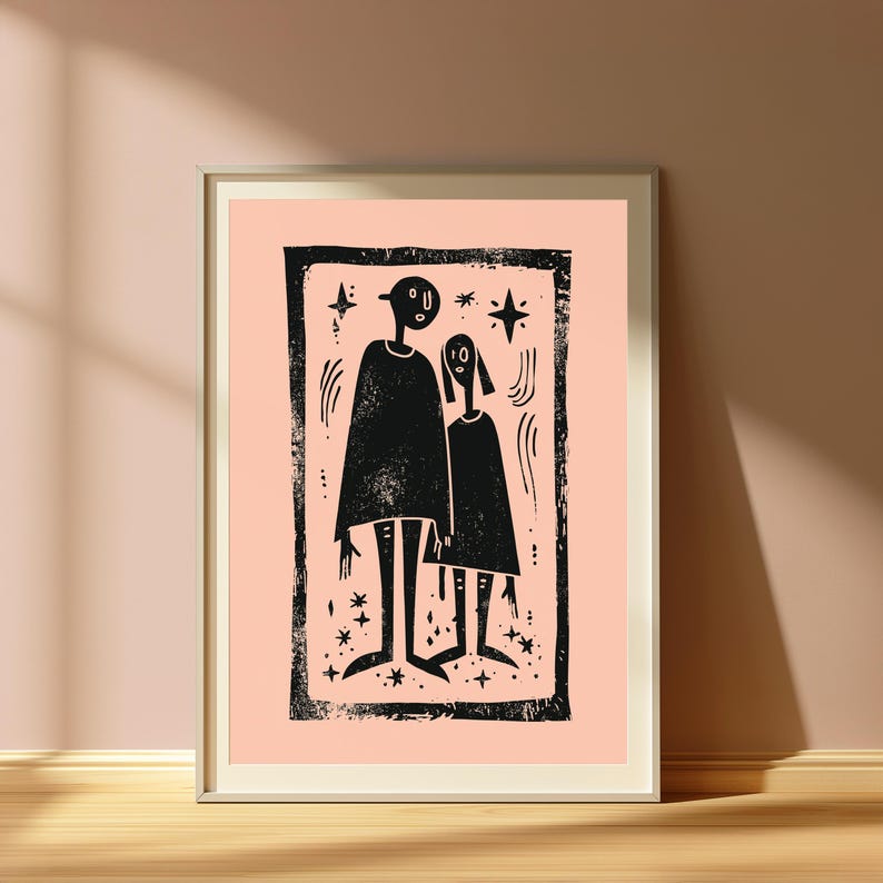 May include: A framed wall art print featuring a black ink block-print style illustration of two stylized figures standing side-by-side. The figures are surrounded by small star shapes and curved lines, all set against a solid light peach background.