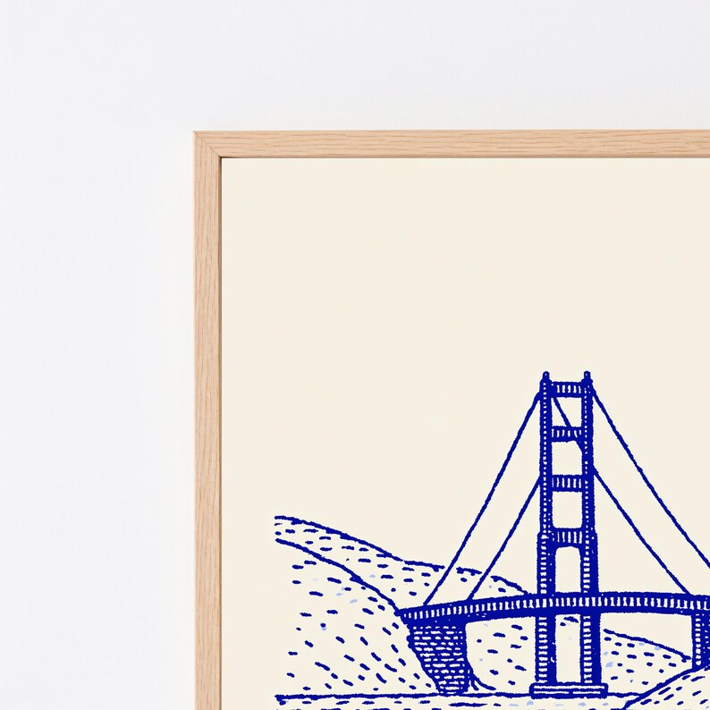 May include: A framed wall art print featuring a blue line drawing of the Golden Gate Bridge on a cream background. The illustration depicts the bridge structure and surrounding hills with a simple, hand-drawn aesthetic inside a light wood frame.