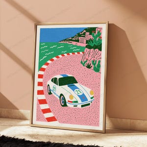 K&ouml;nnte beinhalten: Ein gerahmter Kunstdruck zeigt einen wei&szlig;en Sportwagen mit blauen Rennstreifen und der Nummer 21 auf der Motorhaube und an der Seite. Das Auto f&auml;hrt auf einer rosa Rennstrecke mit rot-wei&szlig;er Begrenzung vor einer K&uuml;stenlandschaft mit gr&uuml;nen Klippen.