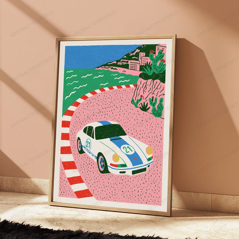 K&ouml;nnte beinhalten: Ein gerahmter Kunstdruck zeigt einen wei&szlig;en Sportwagen mit blauen Rennstreifen und der Nummer 21 auf der Motorhaube und an der Seite. Das Auto f&auml;hrt auf einer rosa Rennstrecke mit rot-wei&szlig;er Begrenzung vor einer K&uuml;stenlandschaft mit gr&uuml;nen Klippen.