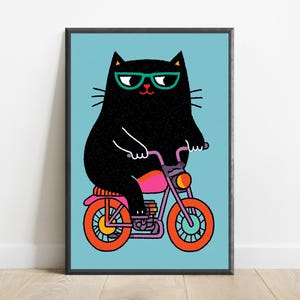 K&ouml;nnte beinhalten: Ein gerahmter Kunstdruck zeigt eine schwarze Katze mit t&uuml;rkisfarbener Brille auf einem lila Motorrad mit leuchtend orangefarbenen R&auml;dern. Die Katze hat ein texturiertes schwarzes Fell und ist vor einem hellblauen Hintergrund grafisch dargestellt.