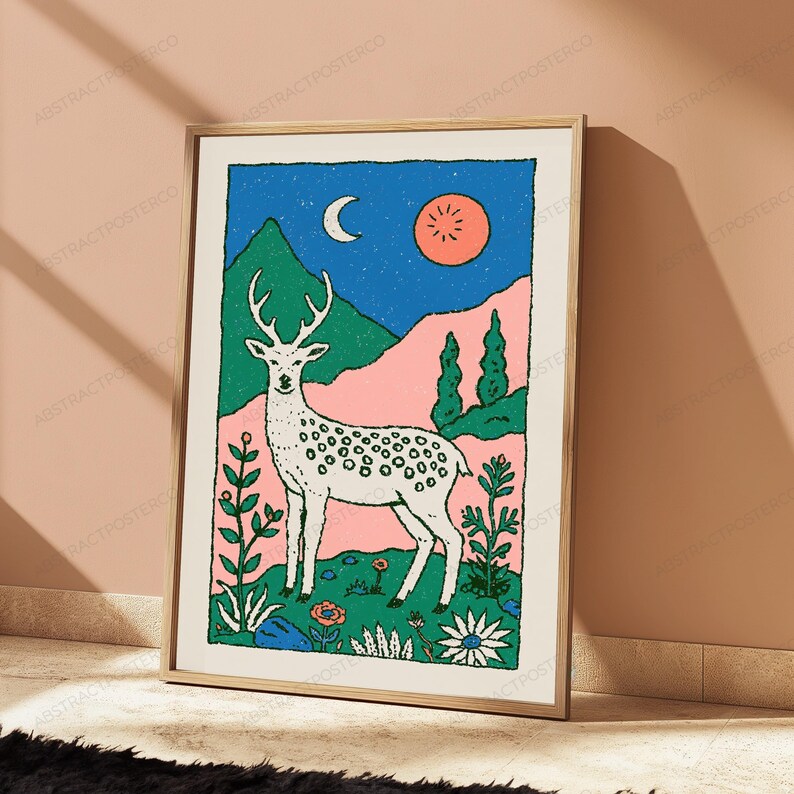 May include: A rectangular wall art print in a light wood frame featuring a stylized illustration of a white spotted deer standing in a field of flowers. The background displays green mountains, a pink landscape, a blue night sky, a crescent moon, and a sun.
