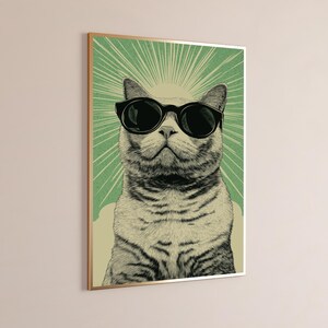 Puede incluir: Una l&aacute;mina de arte mural enmarcada con una ilustraci&oacute;n detallada de un gato atigrado con gafas de sol negras. El gato est&aacute; centrado sobre un fondo verde con l&iacute;neas blancas radiantes, todo ello dentro de un fino marco de color dorado.