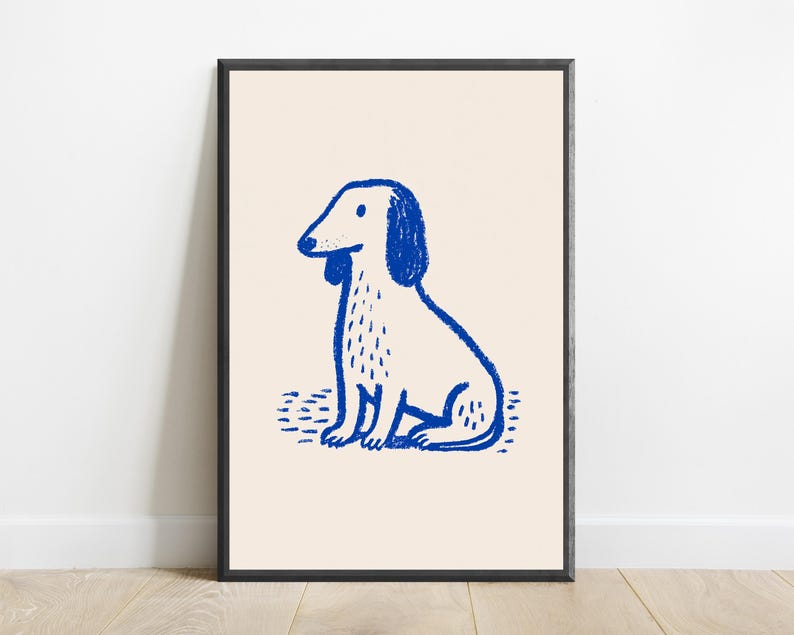 K&ouml;nnte beinhalten: Ein gerahmter Wandkunstdruck mit einer blauen Strichzeichnung eines sitzenden Hundes mit langen Ohren und strukturiertem Fell auf hellcremefarbenem Hintergrund. Die Illustration verwendet einen wachsmalstiftartigen Stil f&uuml;r die Figur.