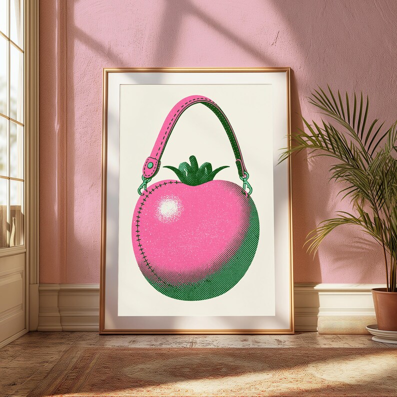 May include: A framed wall art print featuring a stylized illustration of a pink tomato-shaped handbag with a green stem top, a pink handle with green stitching, and a green base, all rendered in a dotted halftone texture on a cream background.