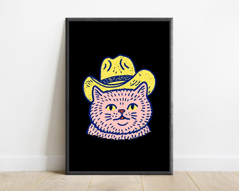 Puede incluir: Una impresi&oacute;n de arte mural enmarcada que presenta una ilustraci&oacute;n gr&aacute;fica de un gato rosa con un sombrero de vaquero amarillo. El gato tiene ojos amarillos y una peque&ntilde;a nariz roja, delineado con trazos negros gruesos sobre un fondo negro.