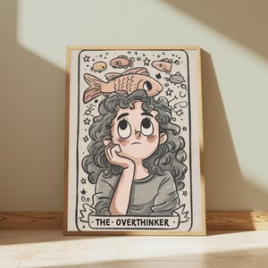May include: A framed art print featuring a cartoon illustration of a person with curly hair resting their chin on a hand. Above their head, several fish and stars are drawn. The text THE OVERTHINKER is printed on a banner at the bottom.