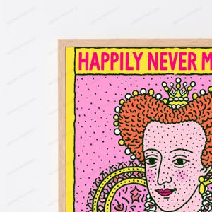 May include: A framed wall art print featuring a stylized portrait of a royal figure with orange hair and a crown, set against a pink background with black dots. The text "HAPPILY NEVER M" is printed in bold pink letters on a bright yellow banner.