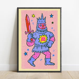 May include: A framed art print featuring a stylized illustration of a knight in blue armor and a crown, holding a red sword. The knight has pink skin and a yellow sun emblem on the chest. The background is light pink with scattered blue and yellow stars.
