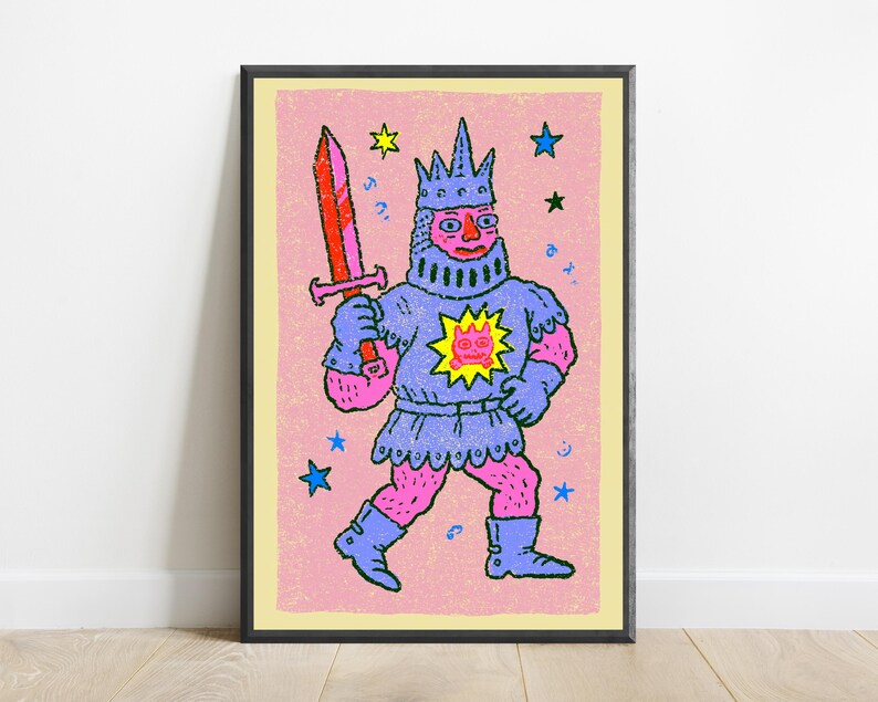 May include: A framed art print featuring a stylized illustration of a knight in blue armor and a crown, holding a red sword. The knight has pink skin and a yellow sun emblem on the chest. The background is light pink with scattered blue and yellow stars.