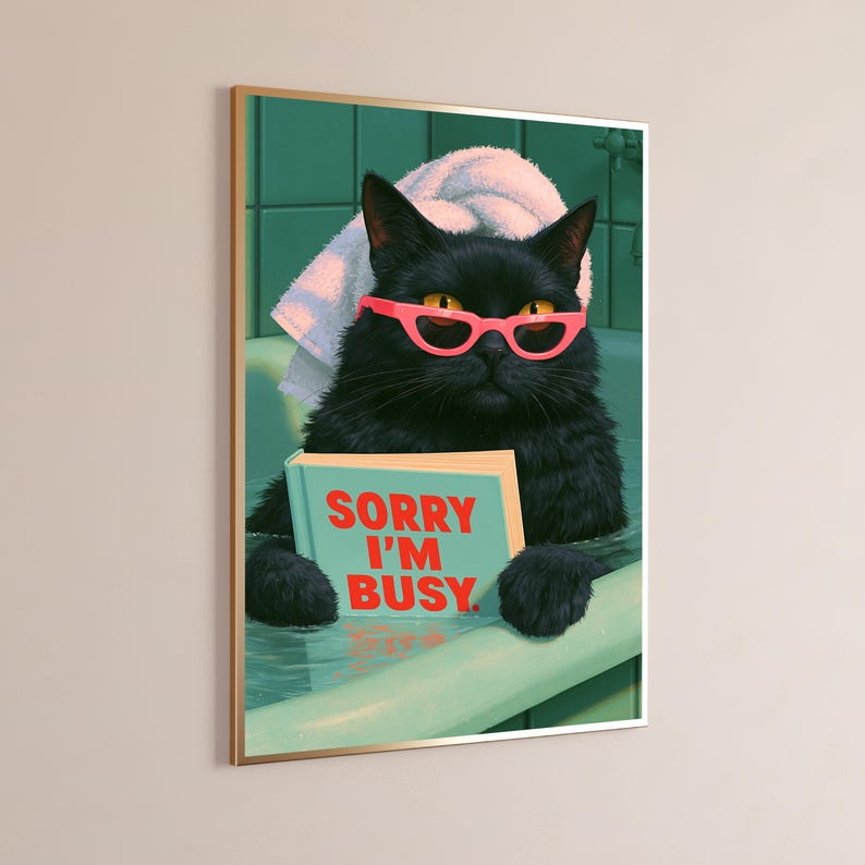 May include: A framed wall art print featuring a black cat in a bathtub with a white towel on its head. The cat wears bright pink cat-eye glasses and holds a light blue book with the red text SORRY I'M BUSY printed on the front cover.