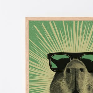 Peut inclure: Une impression d'art encadr&eacute;e repr&eacute;sentant une illustration en gros plan d'un capybara portant des lunettes de soleil noires. L'arri&egrave;re-plan se compose d'un motif en rayons de soleil vert et jaune clair. Le cadre est en bois de couleur claire.