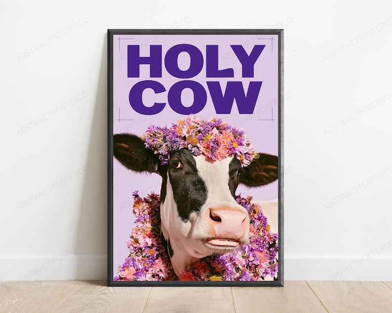 May include: A framed wall art print featuring a black and white cow wearing a colorful floral crown and neck garland. The background is light purple with the bold, dark purple text HOLY COW printed at the top of the rectangular poster.