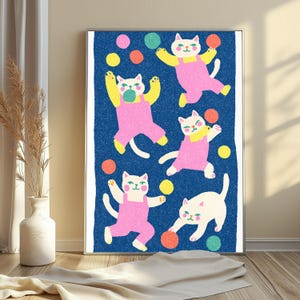 K&ouml;nnte beinhalten: Ein gerahmter Wandkunstdruck mit f&uuml;nf wei&szlig;en Katzen in rosa Latzhosen auf einem strukturierten dunkelblauen Hintergrund. Die Katzen sind in verschiedenen verspielten Posen dargestellt, umgeben von verstreuten bunten Kreisen in Gelb, Orange, Gr&uuml;n und Pink.