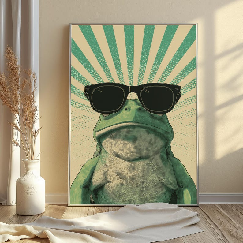K&ouml;nnte beinhalten: Ein rechteckiger Wandkunstdruck, der einen gr&uuml;nen Frosch mit einer gro&szlig;en schwarzen Sonnenbrille zeigt. Der Hintergrund besteht aus einem cremefarbenen Feld mit strahlenden t&uuml;rkisfarbenen Sonnenstrahlen. Der Frosch ist zentriert.