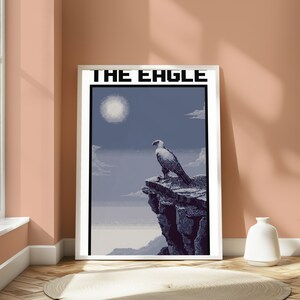 May include: A framed pixel art poster titled THE EAGLE, featuring a white and grey eagle perched on a dark rocky cliff against a blue sky with a bright sun, clouds, and a distant horizon line, all rendered in a distinct digital block style.